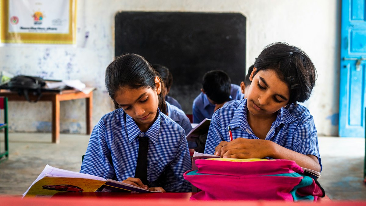 Two schoolgirls reading together at their desks